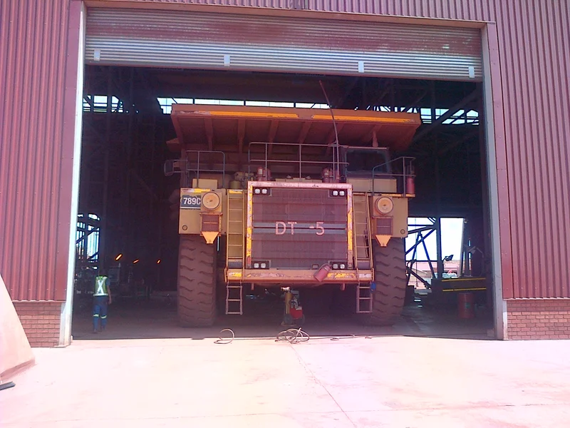A haul truck passing through an oversize roller shutter door, with dimension lines showing its width and height